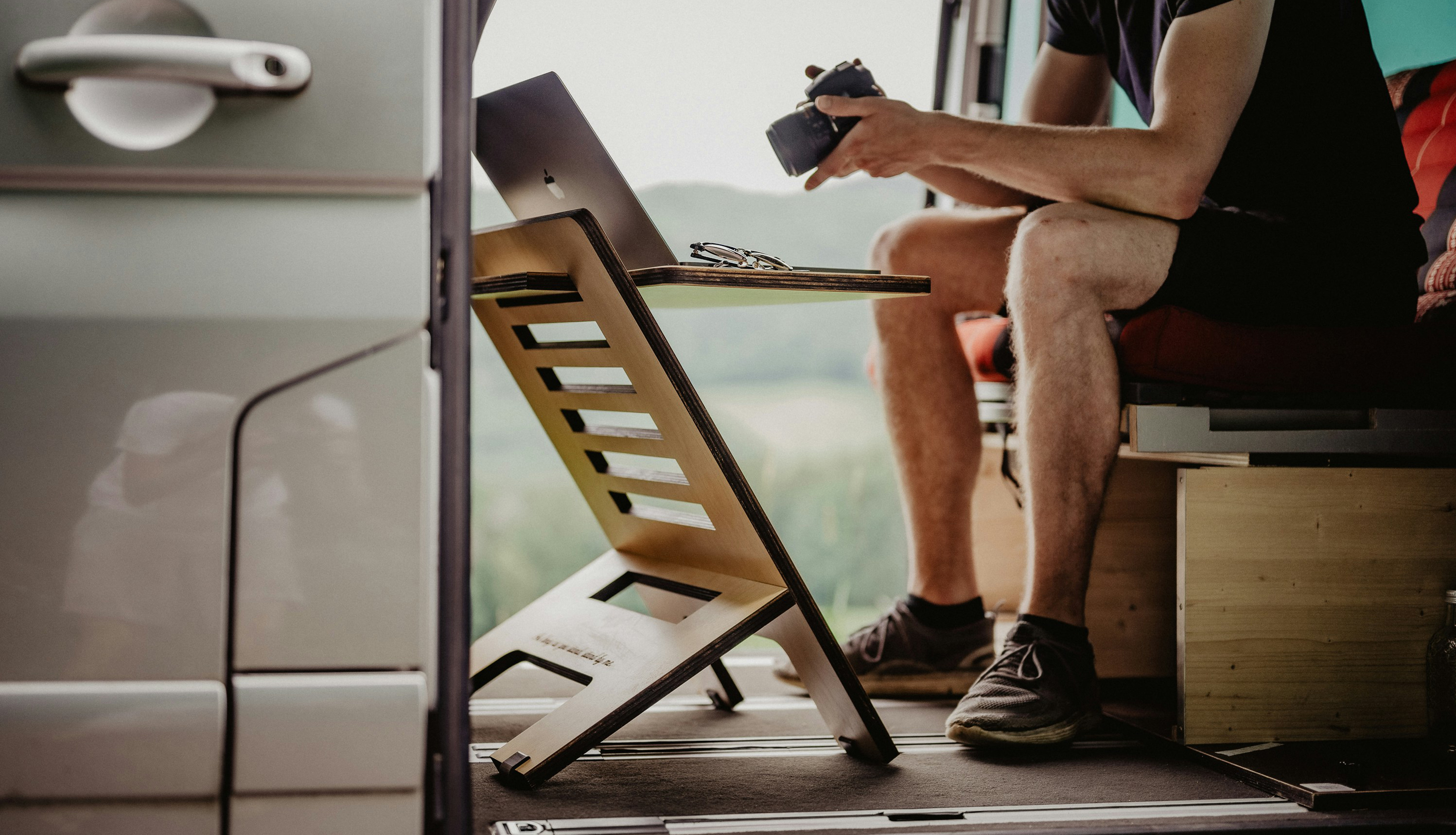 Un voyageur est assis dans son van et regarde l'écran de son appareil photo avec son ordinateur installé sur une petite table en face de lui